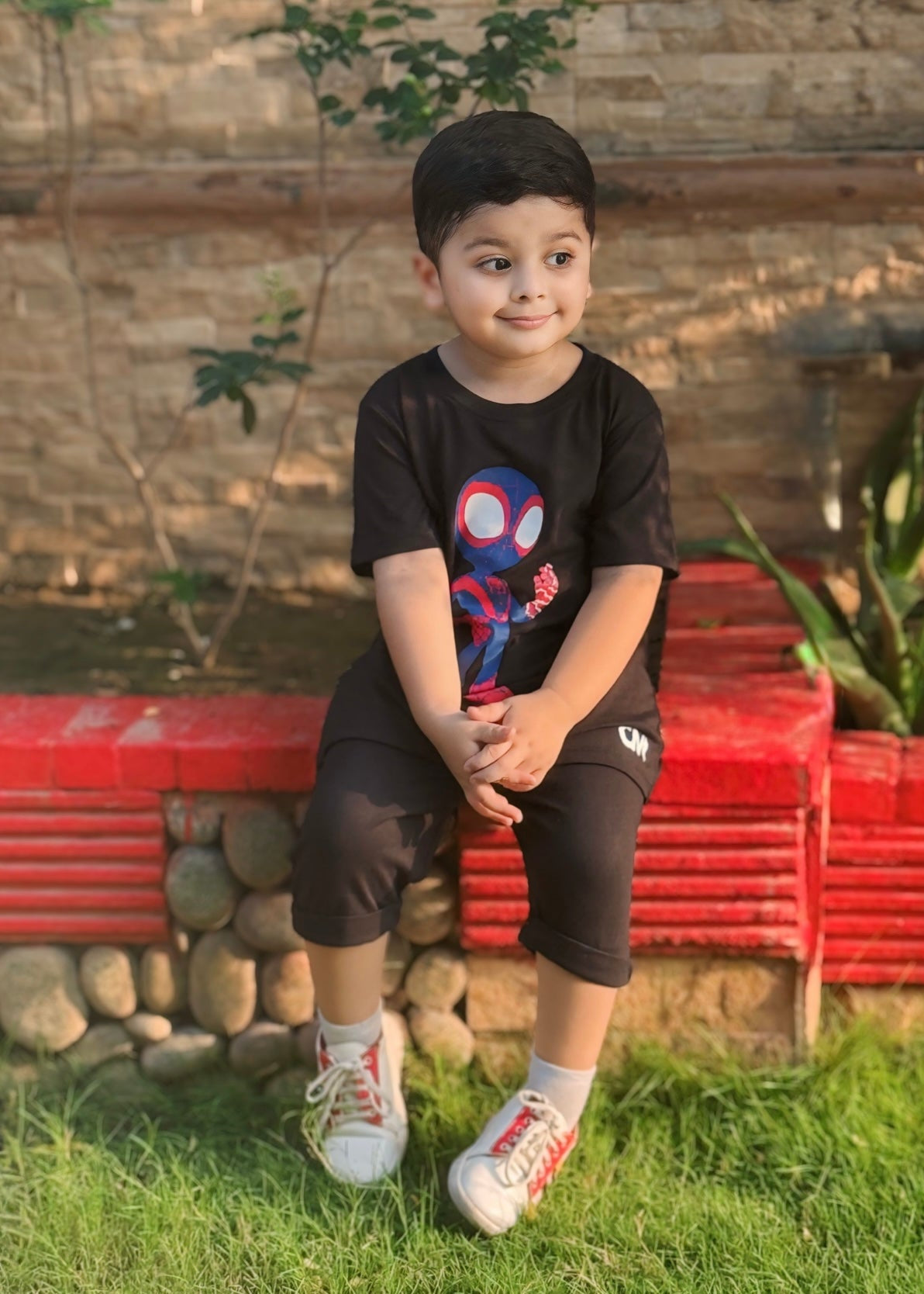 Child wearing a black t-shirt with a colorful design, sitting on a red bench outdoors.