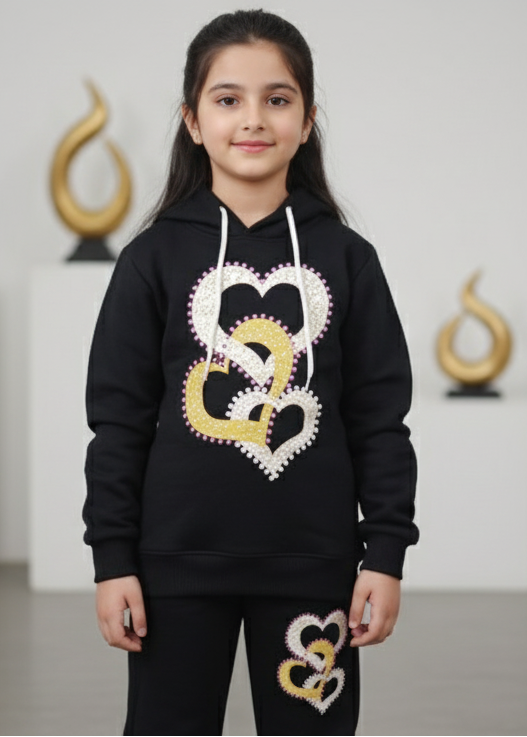 Young girl wearing a black hoodie with heart designs in front of decorative items.