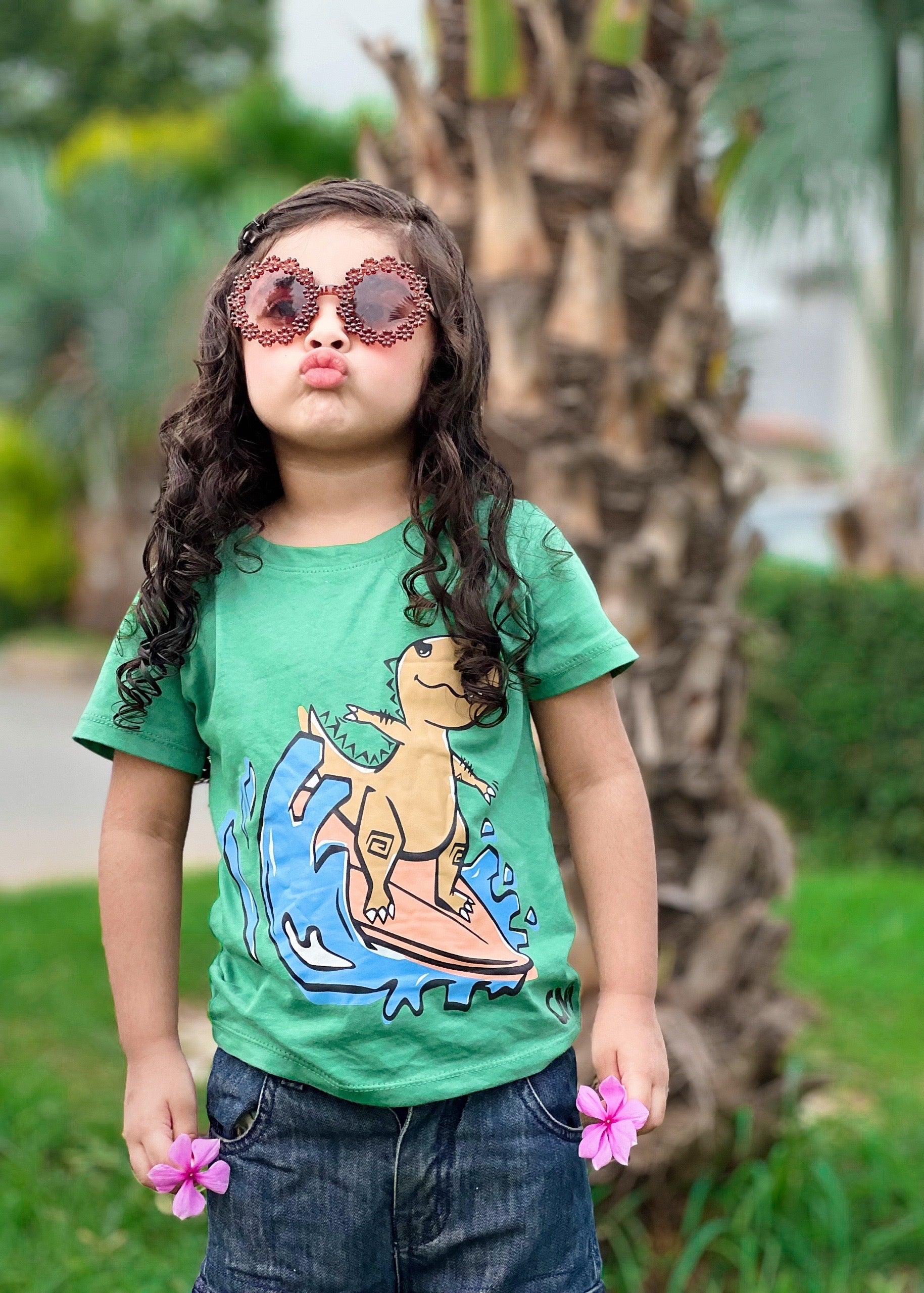 Child wearing a green t-shirt with a graphic design, standing outdoors with trees in the background.
