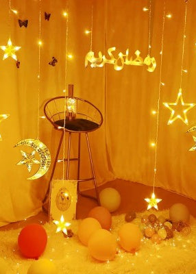 Decorative string lights with stars and moons hanging above a table with balloons and a stool.