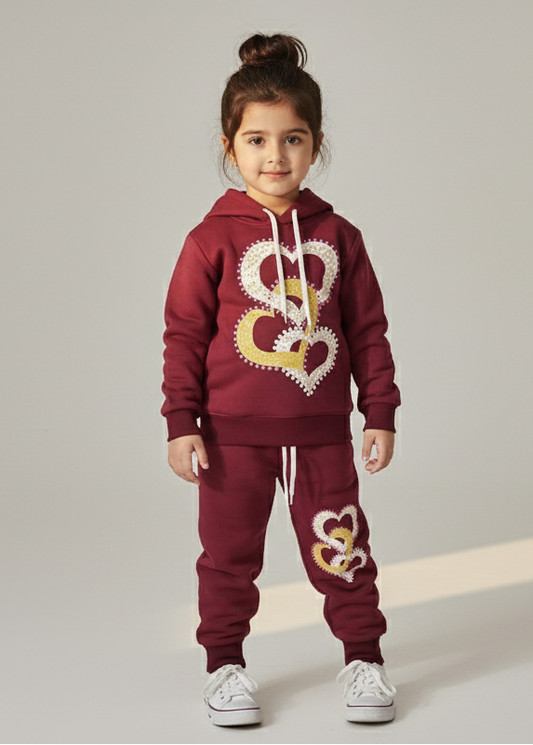 Child wearing a maroon hoodie and pants with heart designs on a light gray background