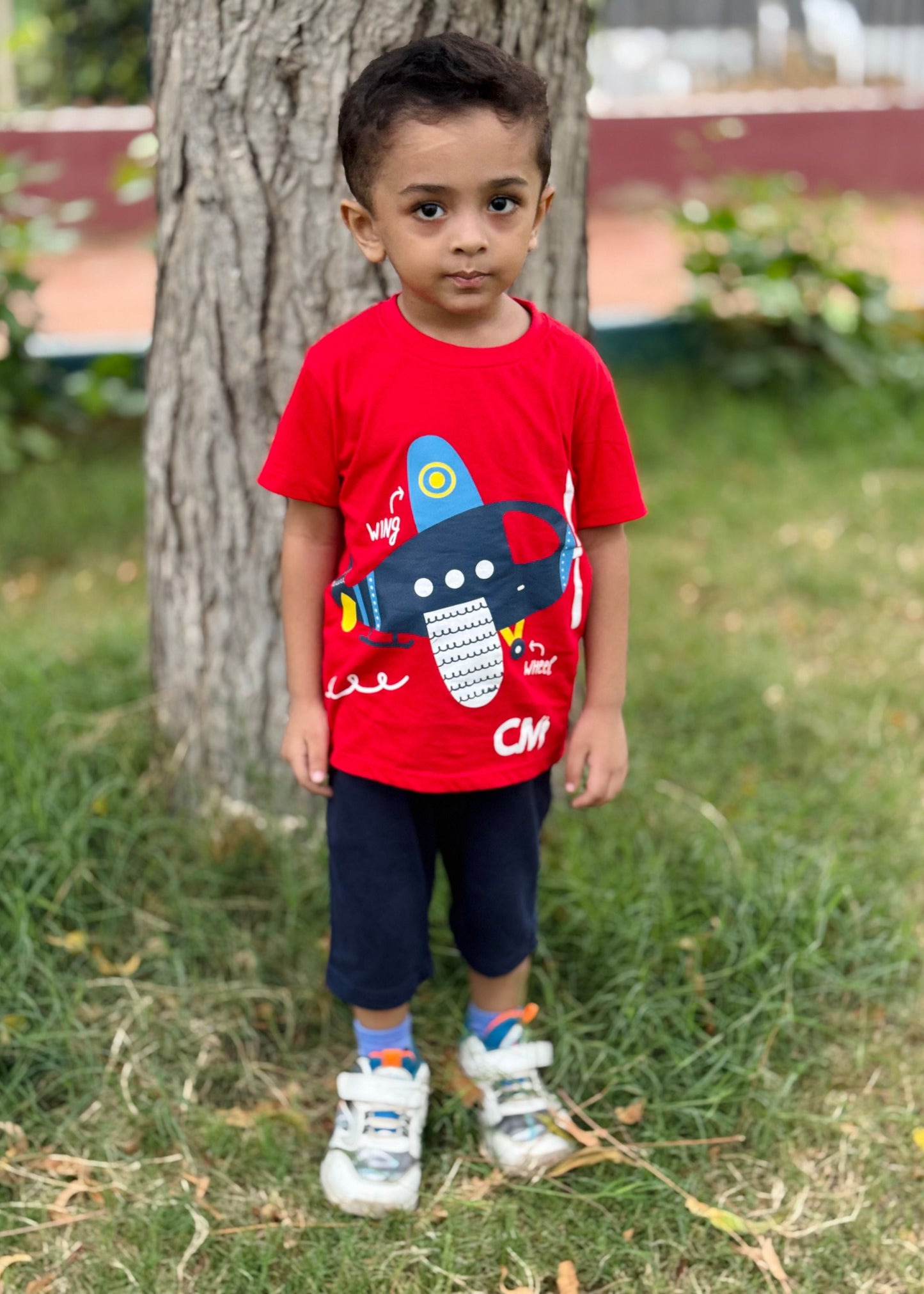 Child wearing a red shirt with a blue airplane design outdoors