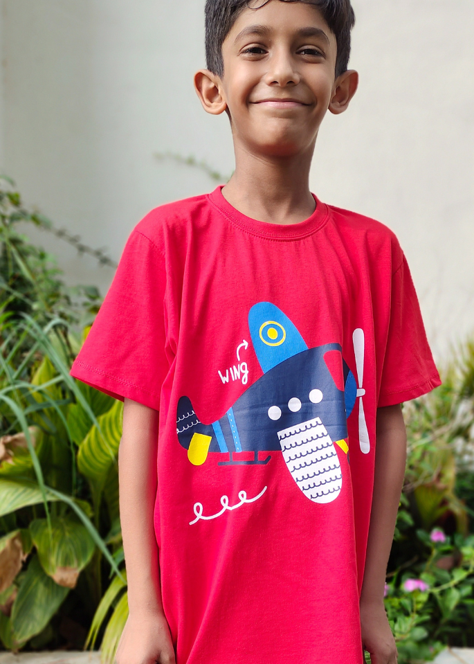 Child wearing a red t-shirt with a blue airplane design outdoors