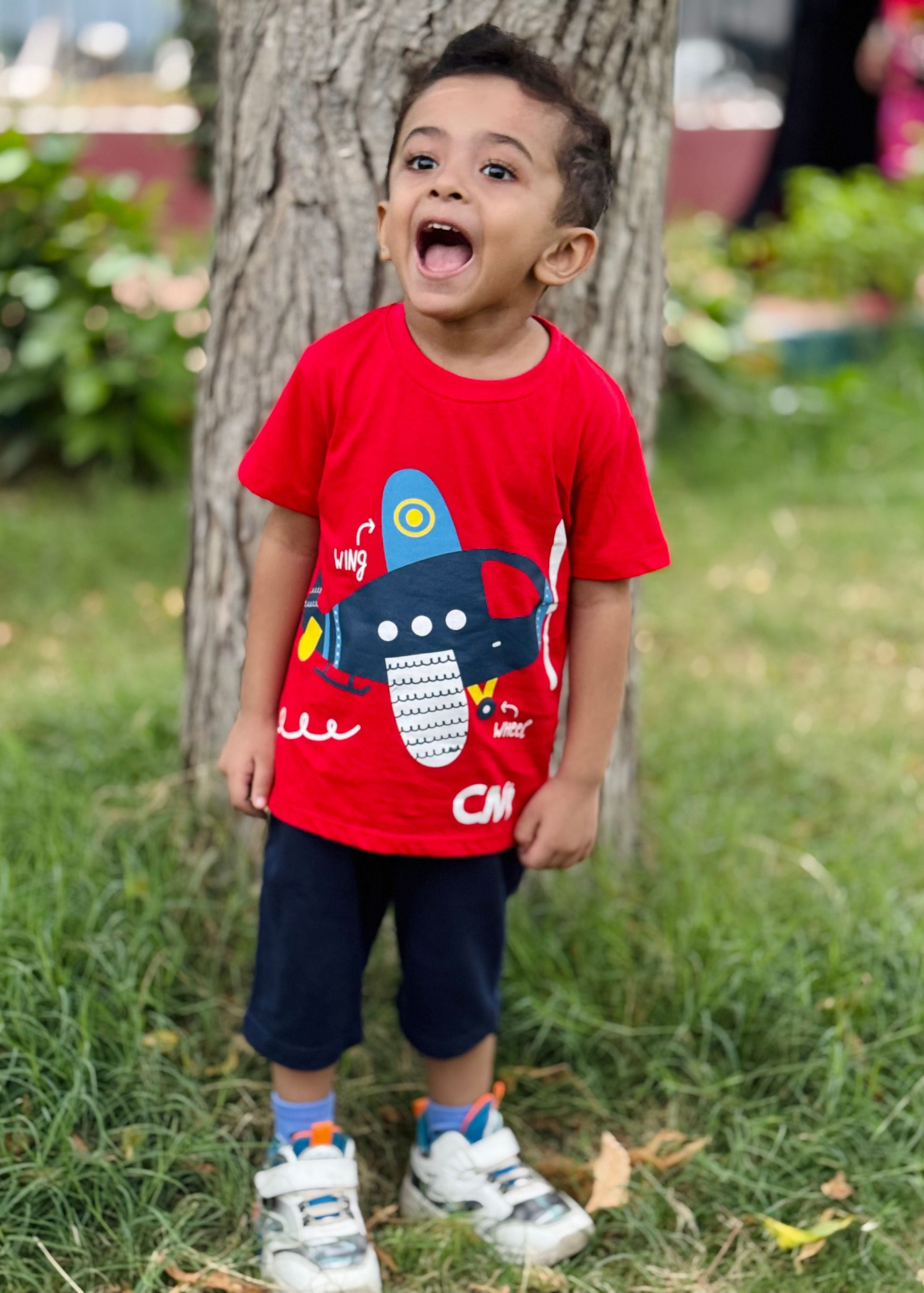 Child wearing a red shirt with a blue graphic design outdoors