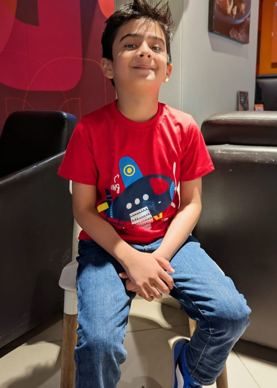 Child wearing a red shirt with a blue graphic sitting on a chair in a colorful room.