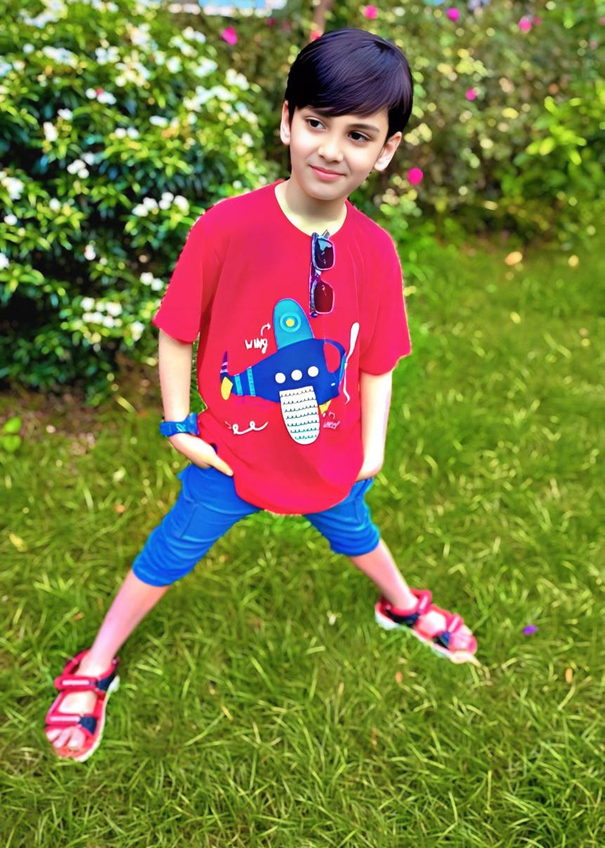 Child wearing a red shirt with a colorful design outdoors on grass