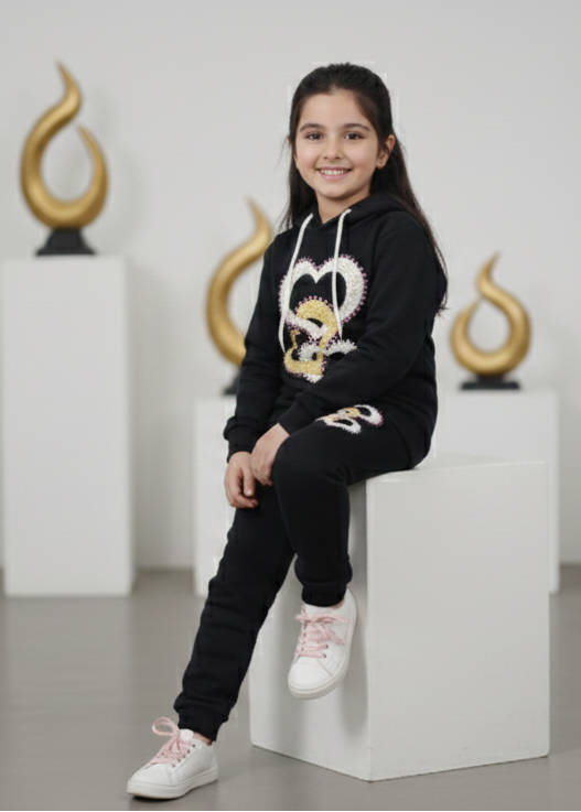 Young girl wearing a black hoodie with a heart design, sitting on a white block in a modern interior setting.