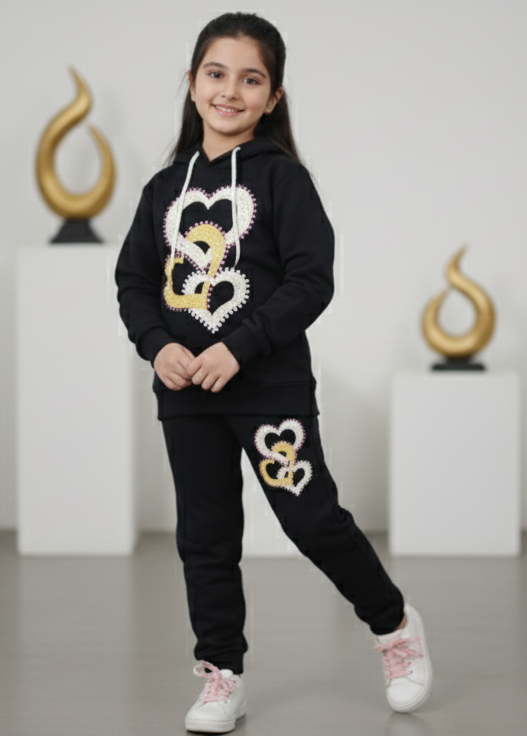 Young girl wearing a black hoodie and pants with heart designs in a minimalistic setting.