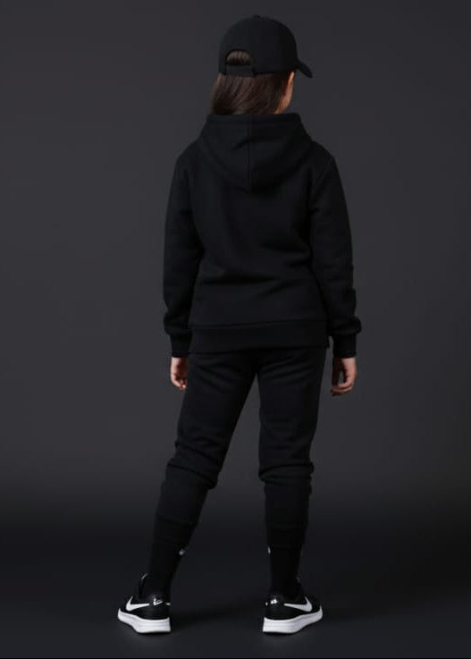 Person wearing a black hoodie and pants with a cap on a dark background