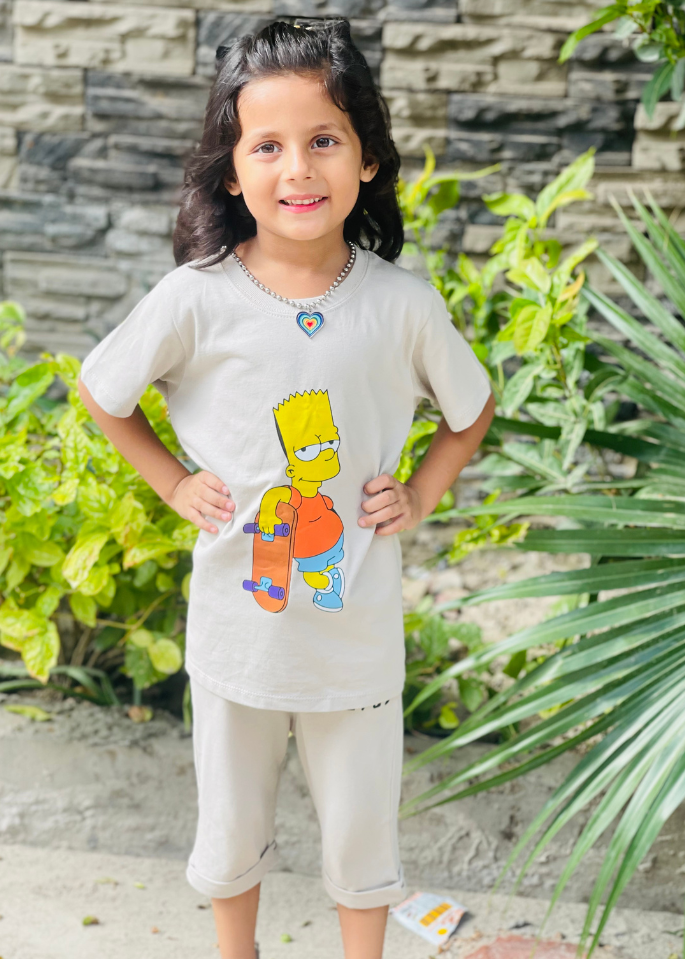Child wearing a shirt with a cartoon character, standing outdoors with greenery and stone wall in the background