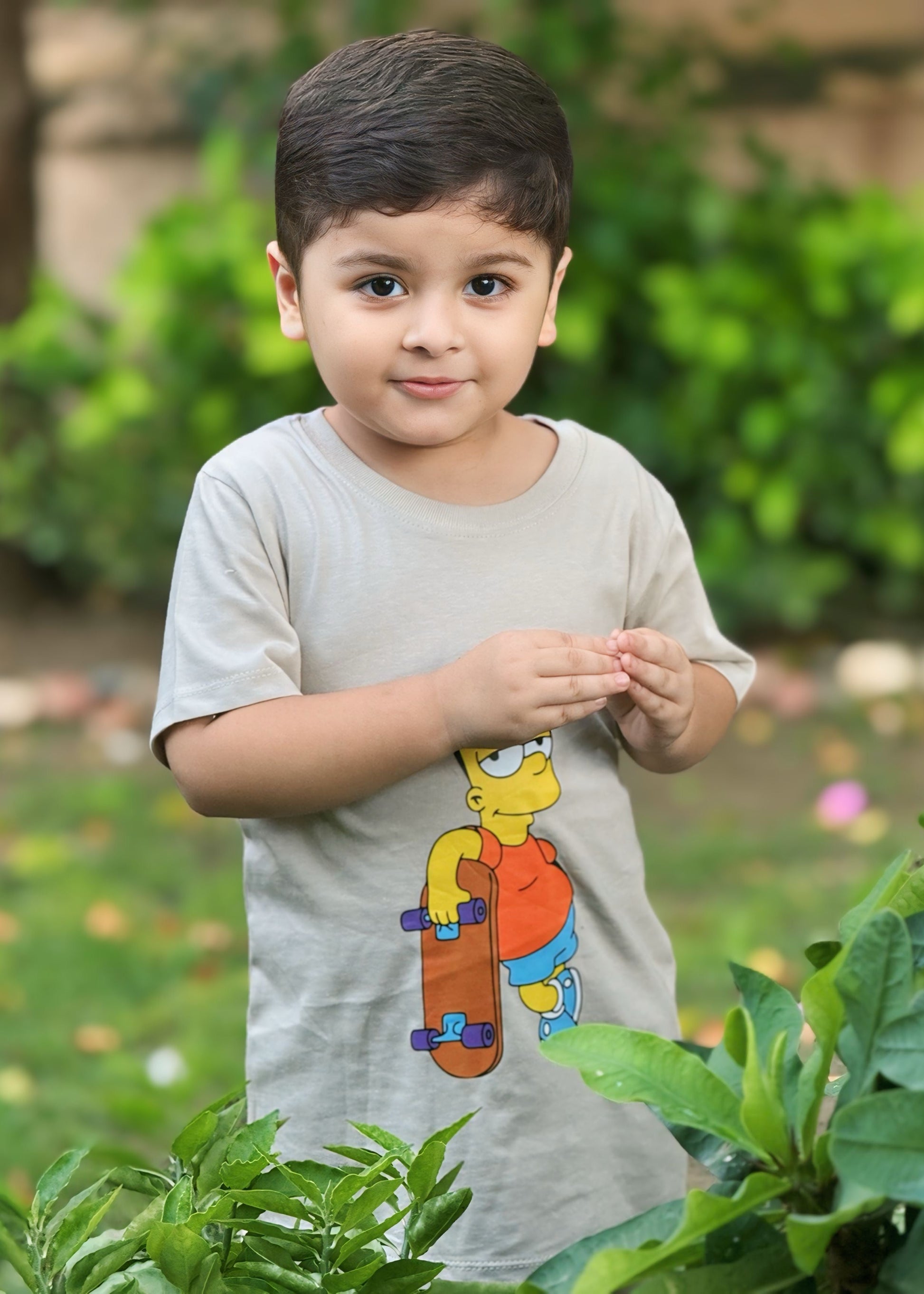 Child wearing a gray t-shirt with a cartoon character, standing outdoors with greenery in the background