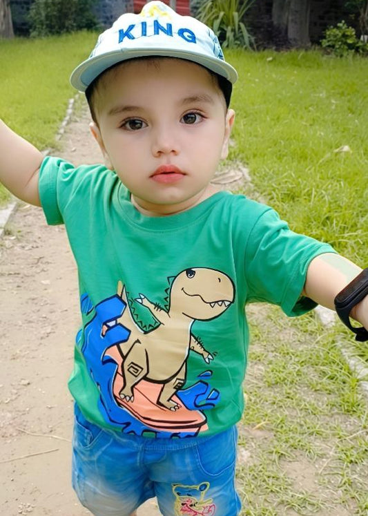 Child wearing a green shirt with a dinosaur design and a white cap outdoors.