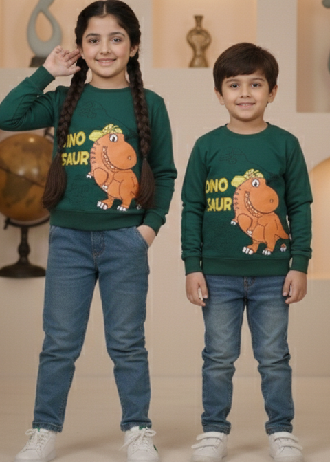 Two children wearing matching green sweatshirts with dinosaur graphics in a decorative indoor setting.