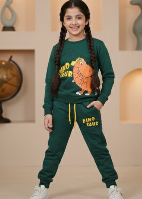 Child wearing a green outfit with a character design, standing in a decorative room with plants and lamps.