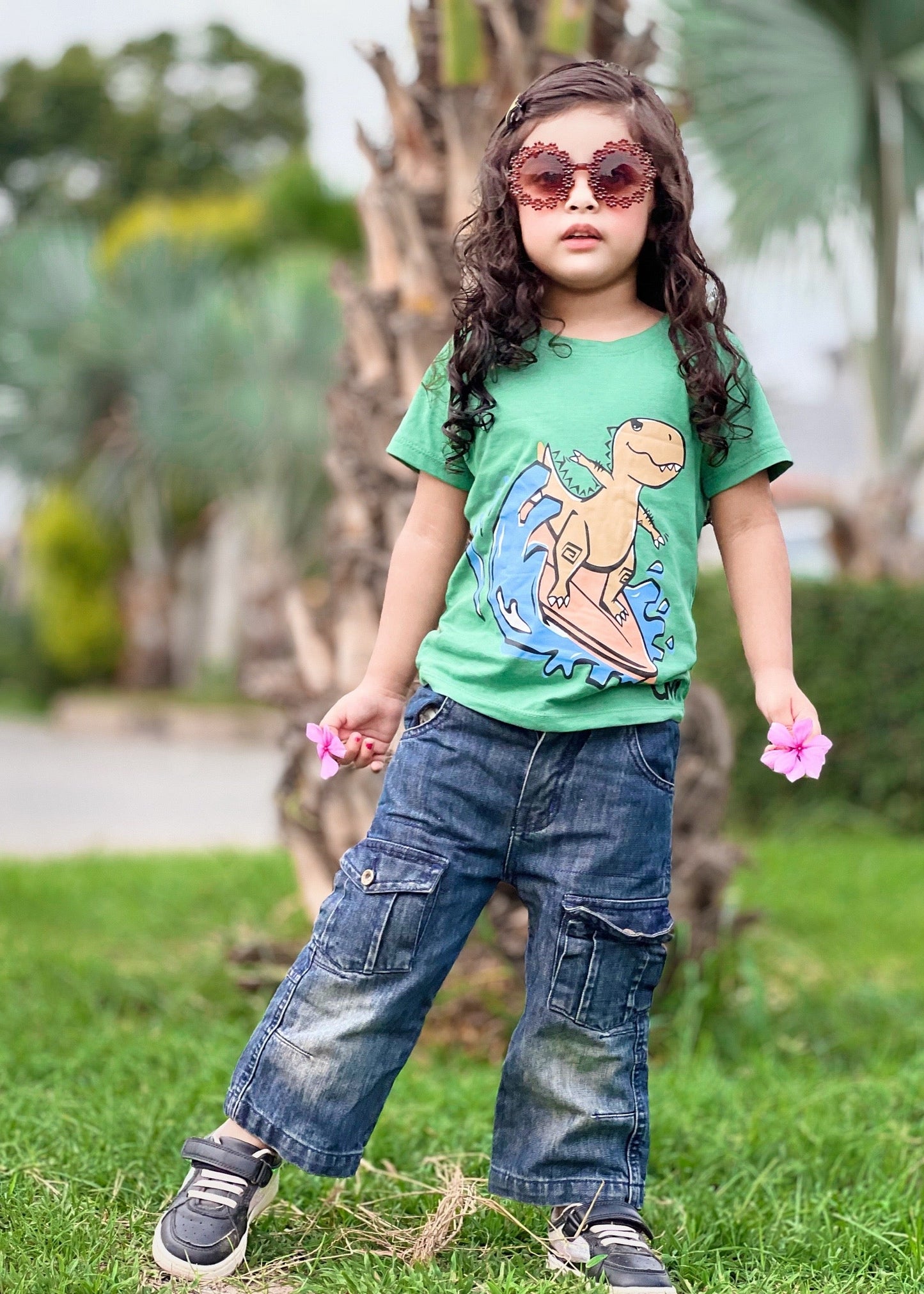Child wearing a green t-shirt with a dinosaur design and blue jeans outdoors.