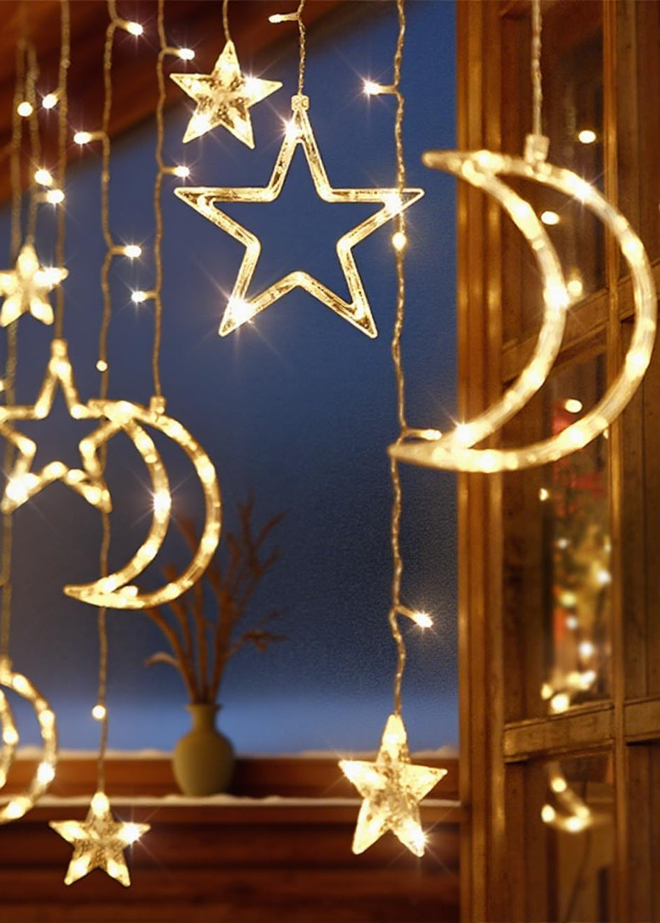 Decorative string lights shaped like stars and moons hanging in front of a window.