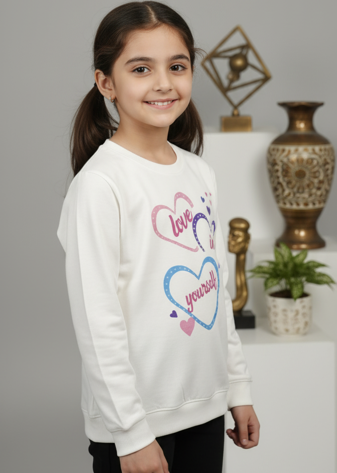 Young girl wearing a white sweatshirt with colorful heart designs against a neutral background