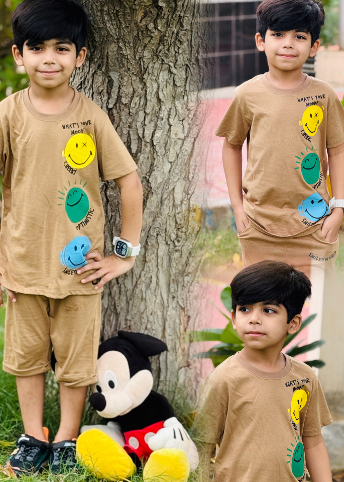 Three children wearing matching outfits with smiley face designs, standing outdoors near a tree.