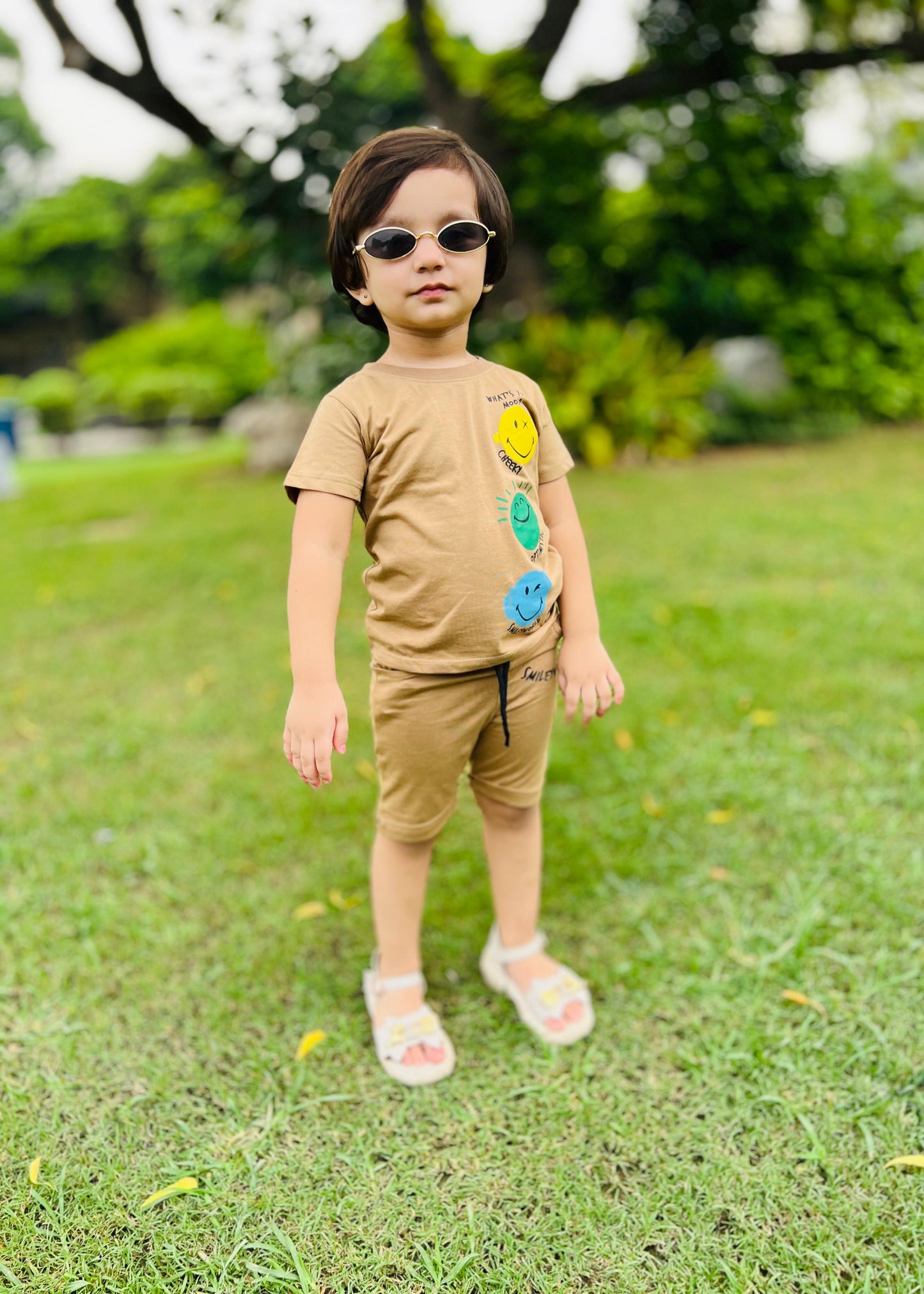 Child wearing a tan outfit with colorful patches standing on grass