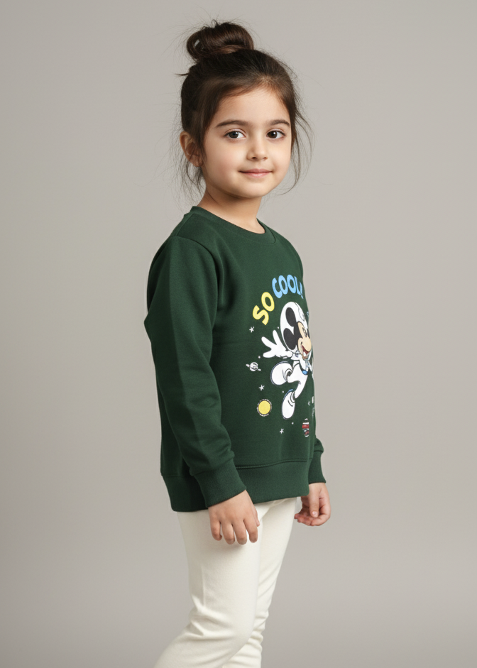 Young girl wearing a green sweatshirt with colorful designs and white pants on a gray background
